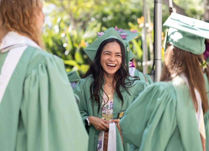 一个学生戴着毕业帽，穿着毕业服，对着朋友微笑